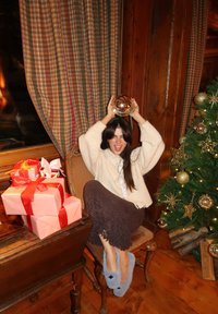 Une chaise en bois avec une personne tenant un objet métallique, entourée de cadeaux enveloppés de papier rose avec des rubans rouges et un sapin de Noël décoré.
