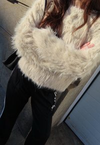 Krämfärgad fluffig tröja med långa ärmar, kombinerad med svarta avsmalnande byxor med vita sidostripes. Texturen ser mjuk och mysig ut.