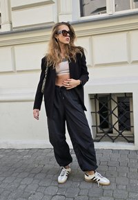 Crni oversized blejzer, skraćeni bež top, široke crne hlače i bijele tenisice s crnim prugama. Dodaci uključuju velike sunčane naočale i torbu.