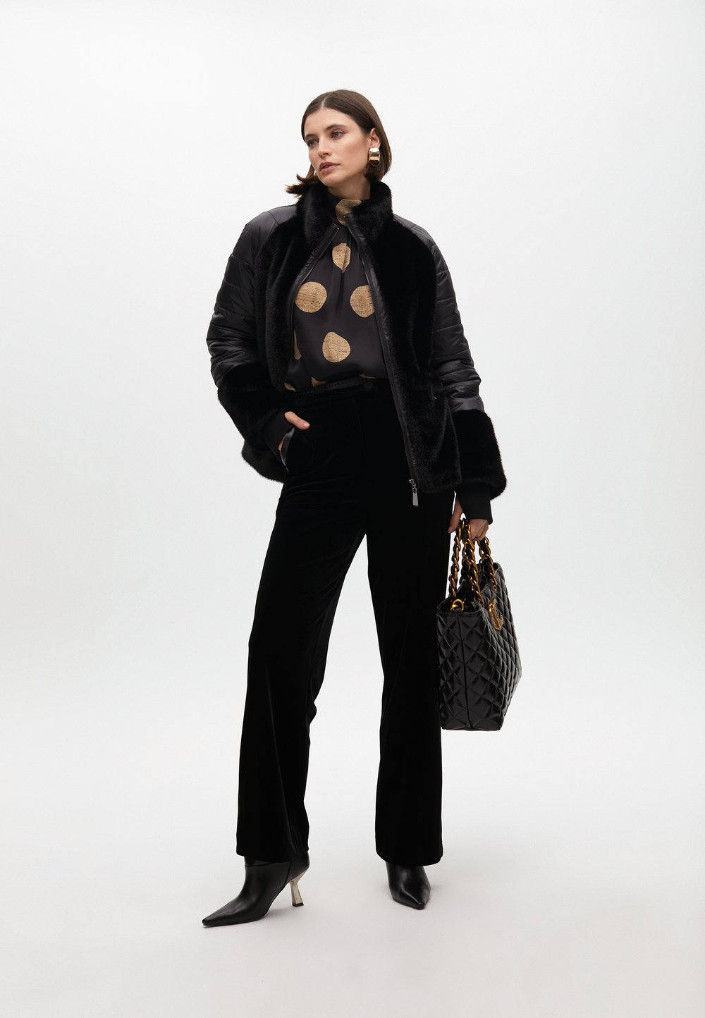 Čierna umelá kožušina na šedej blúzke s veľkými zlatými kruhmi, v kombinácii s čiernymi sametovými nohavicami a špicatými čiernymi opätkami. Obsahuje prešívanú čiernu kabelku.