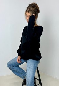 Sweater preto de malha com um painel brilhante, corte oversized e mangas largas, combinado com jeans de perna reta de um azul claro. Textura suave.