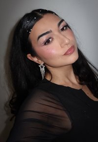 Black sheer long-sleeve shirt, silver star earrings with cascading beads, subtle glitter makeup, and textured dark hair with decorative gems.