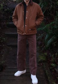 Veste isolée marron avec un col en velours côtelé, assortie à un pantalon en velours côtelé marron et des baskets blanches. Tissu texturé et coupe décontractée.