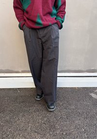 Σκούρο γκρι, παντελόνι φαρδύ με λεία υφή. Συνδυάζεται με μαύρα παπούτσια και φοριέται με μπορντό πουλόβερ που έχει πράσινα γεωμετρικά σχέδια.