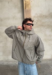 Ruda ir balta languota striukė su aukštu apykakle, užtrauktuku uždarymu ir šoninėmis kišenėmis; derinama su šviesiai mėlynais džinsais.