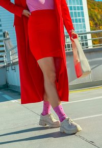 Červená upravená sukně a kabát přes růžový top. Mohutné béžové boty a růžové ponožky se srdíčkovým vzorem. Hladké textury a moderní design.