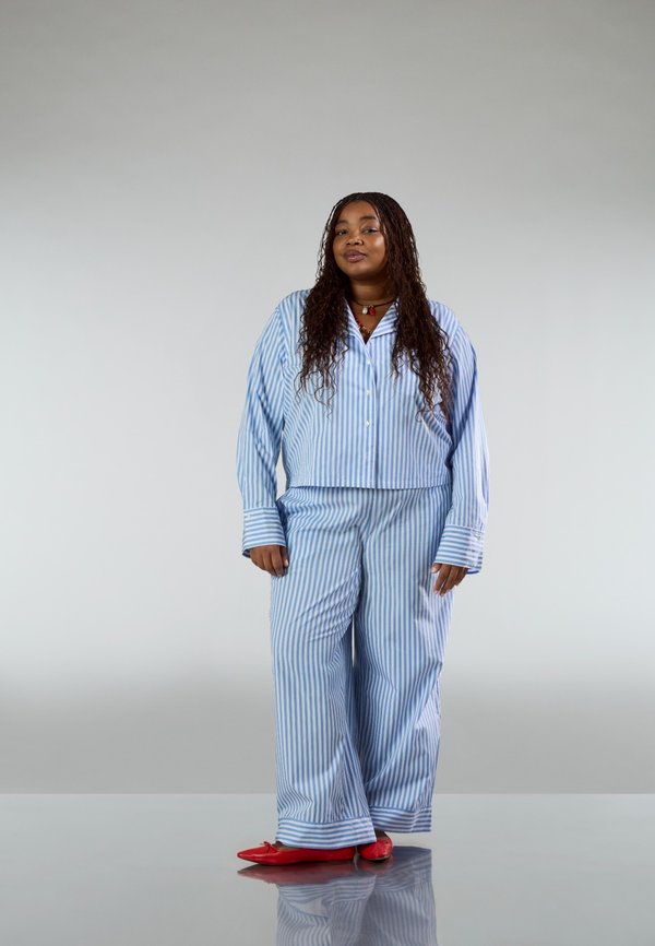 Blauw-wit gestreept pyjamaset met een loszittend shirt en broek met uitslaande pijpen. Rode platte schoenen. Soepele stof, casual ontwerp.