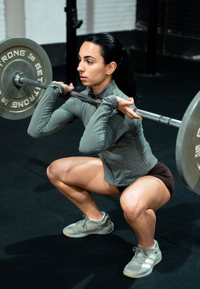 Mujer realizando una sentadilla frontal profunda sosteniendo una barra olímpica sobre sus hombros en un gimnasio.