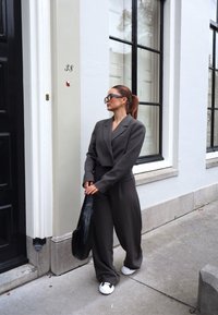 Γκρίζα προσαρμοσμένη σακάκι με ταιριασμένα παντελόνια πουκαμίσας σε φάρδος, φορεμένα με λευκά και μαύρα αθλητικά παπούτσια. Μαύρη τσάντα και υπερμεγέθη μαύρα γυαλιά ολοκληρώνουν την εμφάνιση.