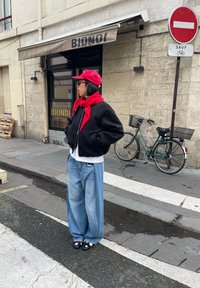Personne portant une casquette et une écharpe rouges, une veste noire et un jean large bleu, debout dans une rue de la ville près d'un vélo et d'un panneau d'interdiction d'entrée devant la boutique BIONDI.
