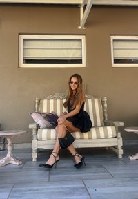 Μαύρες στιλέτο γόβες με λουράκια στο μόριο, μια μαύρη τσάντα χεριού με αλυσίδα και ένα άνετο μαύρο φόρεμα χωρίς μανίκια, είναι τοποθετημένα πάνω σε μια ριγέ καναπέ.