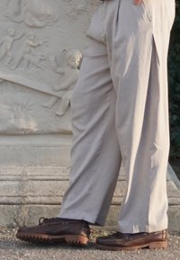 Scarpe casual marroni con suola in gomma testurizzata, abbinate a pantaloni grigi chiari con pieghe, che mostrano una vestibilità ampia e una leggera lucentezza.