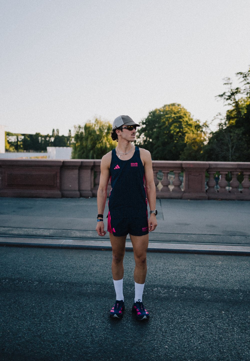 Sportigt set bestående av en marinblå linne med rosa detaljer och matchande shorts, vita strumpor och mörka skor med rosa inslag. Kepa och solglasögon bärs.