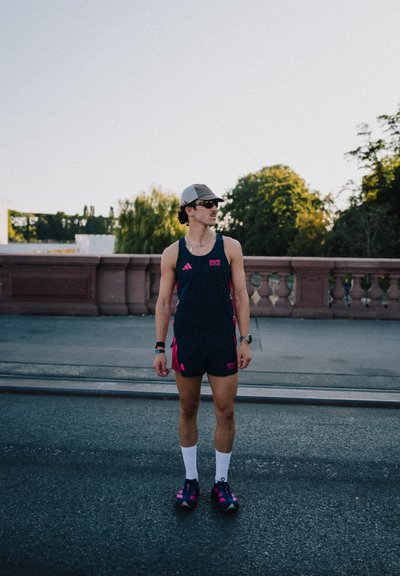 Conjunto atlético que incluye una camiseta sin mangas azul marino con detalles en rosa y pantalones cortos a juego, calcetines blancos y zapatillas oscuras con detalles en rosa. Lleva una gorra y gafas de sol.
