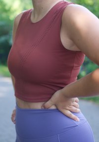Rode sportieve crop top met geperforeerde details, gecombineerd met hoge paarse leggings die een gladde, rekbare textuur hebben.