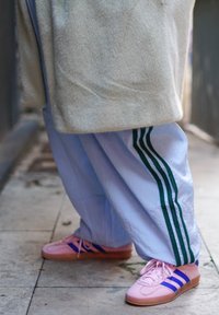 Casaco felpudo cinza claro, calças de treino azuis com riscas verdes e ténis cor de rosa com riscas azuis e sola de borracha.