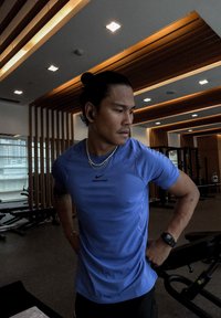 Blå Nike Pro atletisk t-shirt med korte ærmer, båret med sorte atletikbukser. Har et tætsiddende design og synligt logo. Fitnessmiljø.