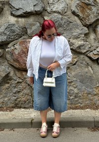 Camisa branca texturizada sobre um top branco ajustado, combinada com calções de ganga largos. Acessórios incluem uma pequena bolsa branca e sapatos cor-de-rosa.
