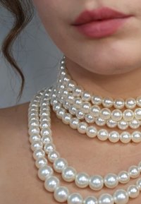 Quattro fili di perle bianche lucide, di dimensioni diverse, disposti in strati attorno al collo, che mettono in mostra una finitura liscia e brillante sulla pelle nuda.