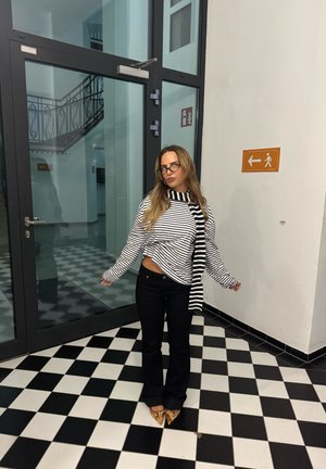 Suéter a rayas con diseño corto, jeans negros acampanados y zapatos puntiagudos con estampado animal. Gafas y una bufanda completan el conjunto.