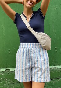 Camiseta de manga corta en color azul marino, pantalones cortos a rayas en azul claro y rosa con cinturilla elástica, y un bolso cruzado beige con cierre de cremallera.