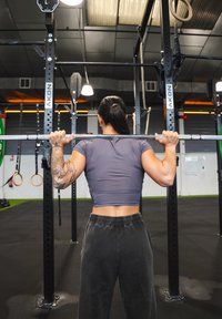 En person i en grå kort t-skjorte og mørke treningsbukser holder en vektstang i et treningsstudio, med forskjellig treningsutstyr i bakgrunnen.