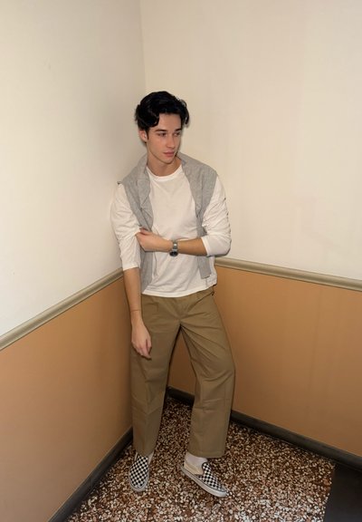 Sudadera gris sobre una camiseta de manga larga blanca, combinada con pantalones caqui y zapatos de slip-on a cuadros en blanco y negro.