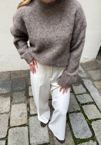 Pull marron duveteux avec un col rond, manches larges, associé à un pantalon large en satin blanc et des chaussures pointues violet foncé.