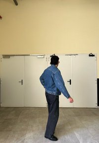 Jeans jakna, svetlo modra, z udobnim krojem in dvema stranskima žepoma. V kombinaciji s temnimi kavbojkami. Nevtralna ozadje z dvojnimi vrati.