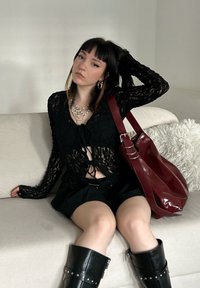 Top de renda preta com mangas longas, design cropped; combinado com uma saia plissada preta e botas pretas até aos joelhos. Mala burgundy. Colar de pérolas.