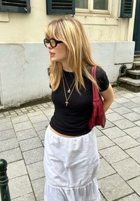 Μαύρο εφαρμοστό μπλουζάκι συνδυασμένο με λευκή φούστα με στρώσεις. Τα αξεσουάρ περιλαμβάνουν χρυσά κολιέ σε στρώσεις και μία κόκκινη δερμάτινη τσάντα.