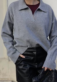 Világosszürke kötött pulóver gallérral és V-nyakkivágással, bordás mandzsettákkal. Fekete bőr sorttal és fonott fekete táskával párosítva.