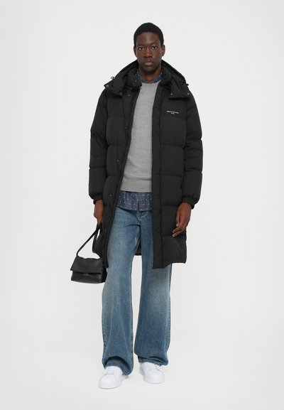 Abrigo de plumas negro con capucha, suéter gris, camisa azul con estampado, jeans claros de pierna ancha y zapatillas blancas, sosteniendo un pequeño bolso negro.
