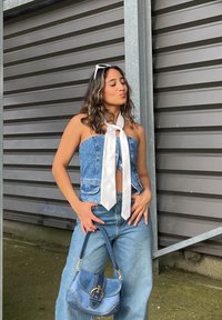 Denim top bez ramienok s bielym saténovým viazaním, skombinovaný s džínsami s širokými nohavicami a malou džínsovou kabelkou s doplnkami zlatého kovu.
