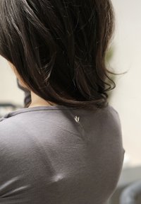 Cheveux noirs courts reposant sur le dos d'une personne portant un haut gris avec une petite déchirure près de l'encolure.