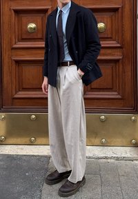 Tamsiai mėlynas dublikinis švarkas, šviesiai mėlyna marškiniai, rudas kaklaraištis, smėlio spalvos klostuoti kelnių, ir tamsiai rudi batai. Medinis fonas su auksiniais akcentais.