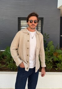 Bēša ribota džemperjakas ar lielām pogām, valkāts virs baltas T-kreklu, kopā ar tumši ziliem džinsiem. Aksesuāri: apaļas saulesbrilles.