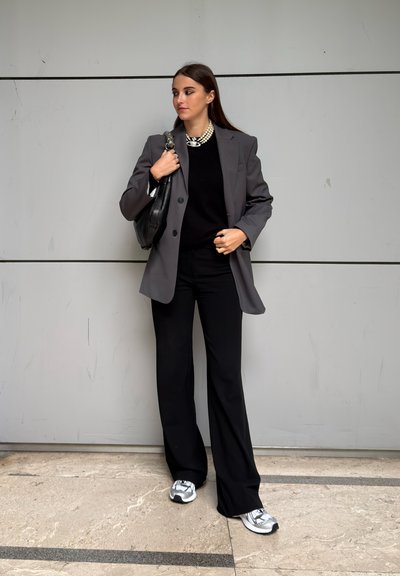 Blazer gris sobre un suéter negro, combinado con pantalones negros de pierna ancha y zapatillas con detalles plateados. Incluye bolso negro y collar de perlas.