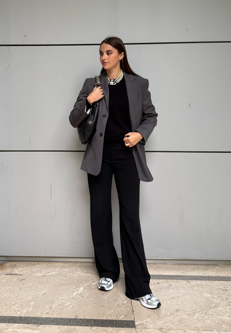 Gray blazer over a black sweater, paired with black wide-leg trousers and silver-accented sneakers. Black handbag and pearl necklace included.