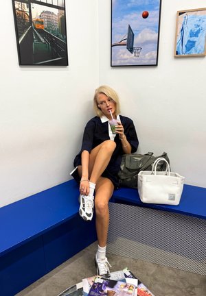 Vestido camisero de gran tamaño en color navy con cuello blanco, combinado con zapatillas blancas y calcetines hasta la pantorrilla. Bebida verde en la mano, junto a bolsas grises y blancas.