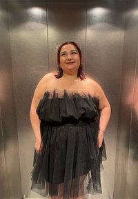 Robe noire sans bretelles avec un corsage et une jupe en tulle superposés. La texture est douce avec un aspect transparent et fluide. Arrière-plan argenté.