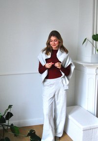 Helle graue Jogginghosen und eine passende Wickeljacke über einem burgunderfarbenen Oberteil. Einfaches Design, weiche Textur und lässige Passform. Warme, gemütliche Umgebung.