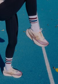 Apavu augšdaļa ir gaiši bēša un mauves krāsā, ar biezu baltu zoli un izteiksmīgu logotipu. Valkāts kopā ar melnām sporta biksēm un svītrainām zeķēm.