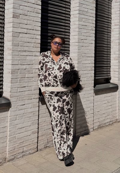 Chándal ligero con patrón de vaca en blanco y negro, que incluye una chaqueta con cremallera y pantalones de pierna ancha. Se complementa con un accesorio negro suave.