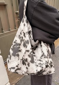 Grå og sort mønstret stoftaske med en slasket form og bred rem, der har et stort, rummeligt rum og syninger som detaljer.