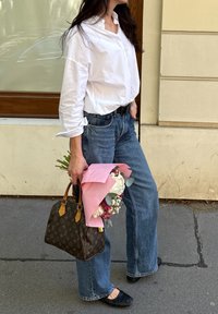 Fehér gombos ing, kék, bő szárú farmernadrág, egy barna Louis Vuitton táskával és egy rózsaszín papírba csomagolt csokorral. Fekete lapos cipő.