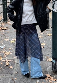 A layered tartan skirt in sheer navy with blue accents, paired with light blue wide-legged jeans and black pointed shoes.