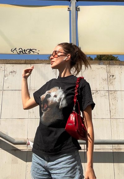Camiseta negra con un gran gráfico de un perro ladrando, combinada con pantalones cortos de mezclilla azul claro y un pequeño bolso rojo de hombro.