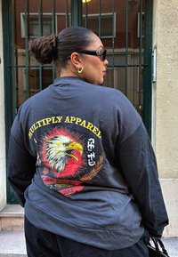 Svart langermet skjorte med et fargerikt ørner motiv på ryggen, med teksten "MULTIPLY APPAREL" og dekorative detaljer.