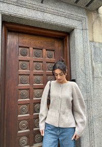 Cardigan grigio chiaro in maglia con scollo arrotondato, texture a coste e maniche lunghe a sbuffo; presenta due bottoni e tasche laterali.